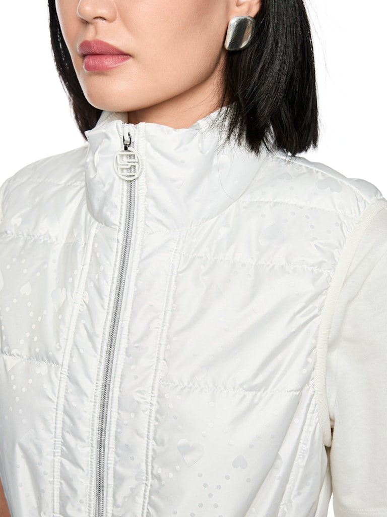 וסט מרופד בעיצוב ספורטיבי, עם הדפס בדוגמת לבבות. גזרה ישרה, עם שרוכי גומי מתכווננים במותניים להתאמה אישית, צווארון עומד, כיסים צדדיים הניתנים לסגירה, ורוכסן דו כיווני, בגימור מנג'ט ארוג בדוגמת פסים צבעוניים.הרכב: 65% פוליאמיד, 35% פוליאסטרהדוגמנית בגובה 1.79 ולובשת מידה 3 של מארק קיין