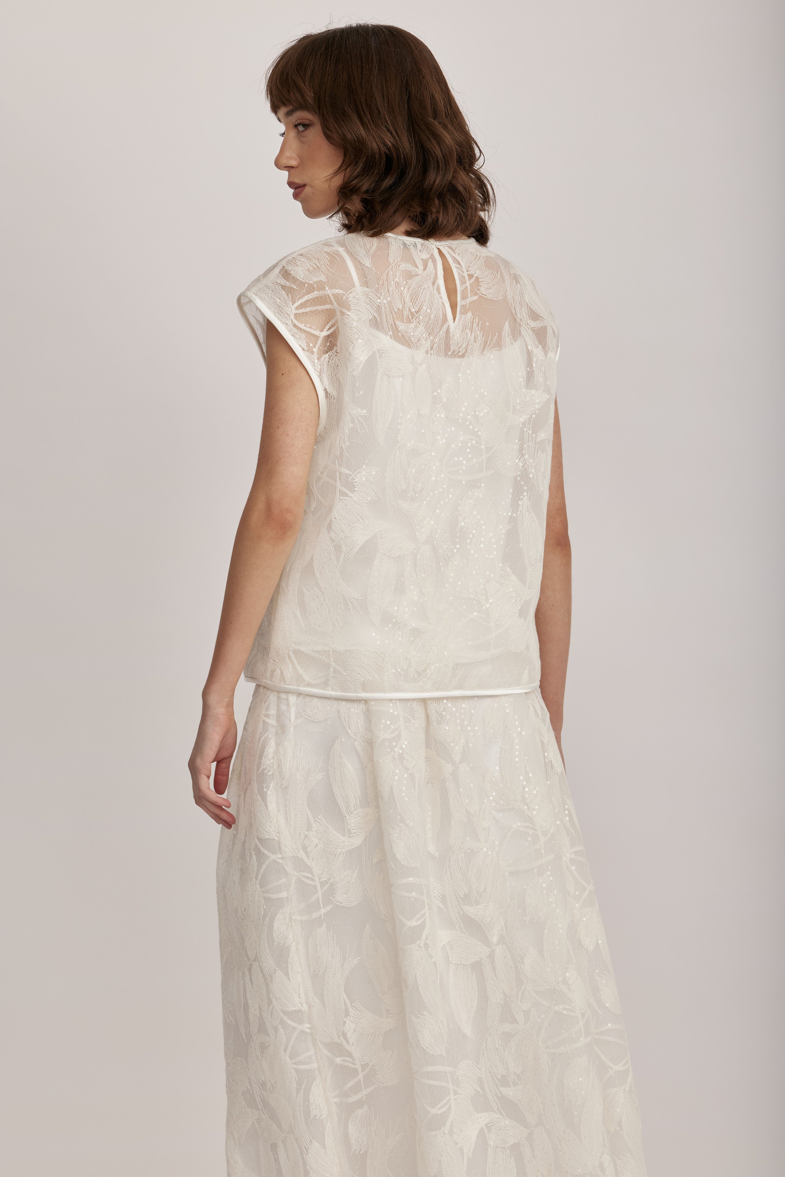 חולצה מקולקציית ה-Runway של המותג האיטלקי PESERICO, בעיצוב דו-שכבתי המשלב בד טול שקוף מעוטר ברקמה עדינה עם פאייטים בדוגמת עלים, ובד אורגנזה דק וקליל בגוון תואם, היוצר משחקי טקסטורה ושקיפויות, ומראה ייחודי.החולצה בגזרה ישרה ומשוחררת, עם שרוולי קאפ קצרים, צווארון עגול, בטנה פנימית, וסגירה באמצעות כפתור בגב.הרכב: טול- 50% פוליאמיד, 50% כותנה, אורגנזה- 100% פוליאסטר, בטנה- 97% פוליאסטר, 3% אלסטןהדוגמנית בגובה 1.75 ולובשת מידה 42 של PESERICO