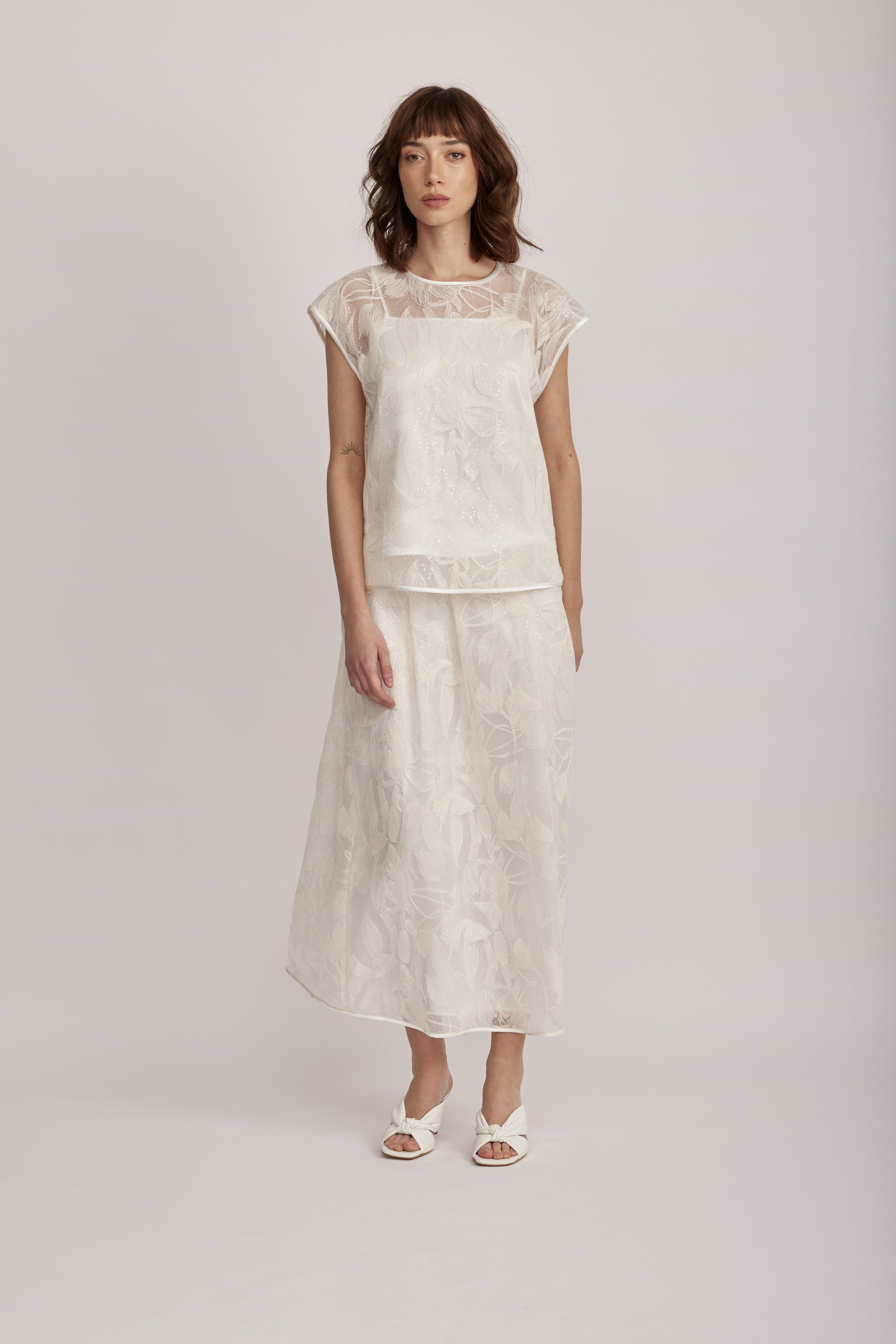 חולצה מקולקציית ה-Runway של המותג האיטלקי PESERICO, בעיצוב דו-שכבתי המשלב בד טול שקוף מעוטר ברקמה עדינה עם פאייטים בדוגמת עלים, ובד אורגנזה דק וקליל בגוון תואם, היוצר משחקי טקסטורה ושקיפויות, ומראה ייחודי.החולצה בגזרה ישרה ומשוחררת, עם שרוולי קאפ קצרים, צווארון עגול, בטנה פנימית, וסגירה באמצעות כפתור בגב.הרכב: טול- 50% פוליאמיד, 50% כותנה, אורגנזה- 100% פוליאסטר, בטנה- 97% פוליאסטר, 3% אלסטןהדוגמנית בגובה 1.75 ולובשת מידה 42 של PESERICO