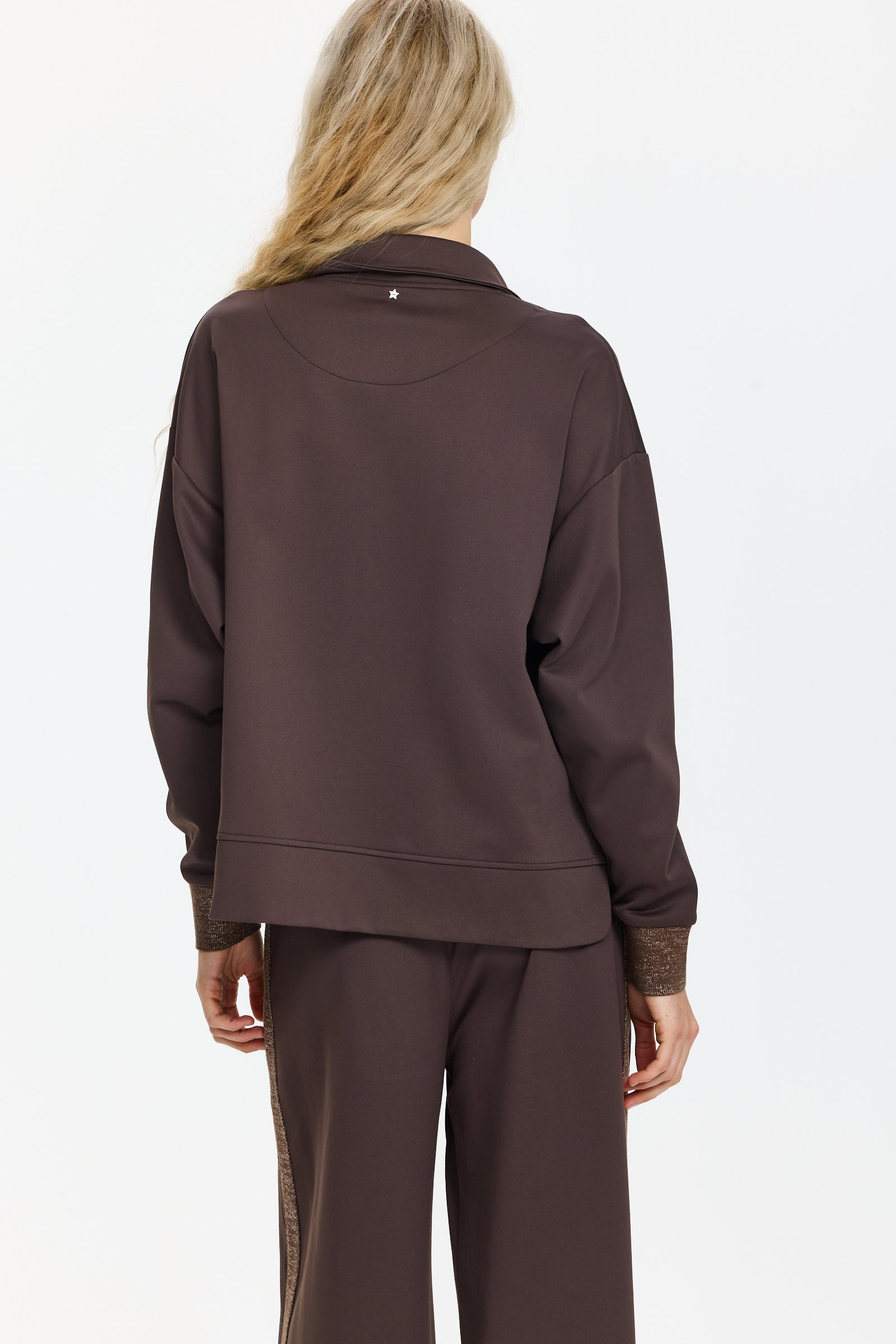 סווטשירט בצבע חום כהה עם צווארון גבוה, רוכסן כפול, כיסים קדמיים וכוכב בגב, קצוות השרוולים נוצציםהדוגמנית בגובה 1.75 ולובשת מידה 40 של Lorena Antoniazzi