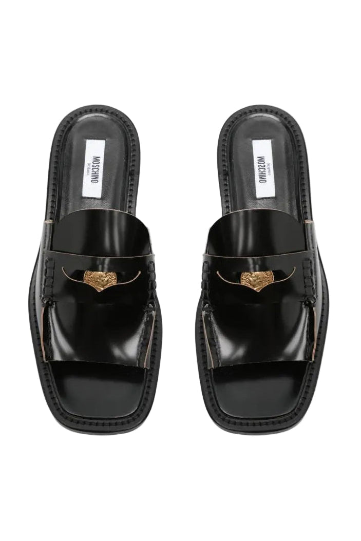 כפכפים מבית המותג האיטלקי MOSCHINO, בסגנון כפכפי מיולז.החלק העליון עשוי עור איכותי, עם עיטור מטבע מוזהב. סוליית גומי עם חרטום מרובע, רפידת עור, ועקב בלוק נמוך.גובה עקב: 2 ס"מהרכב: 100% עור
