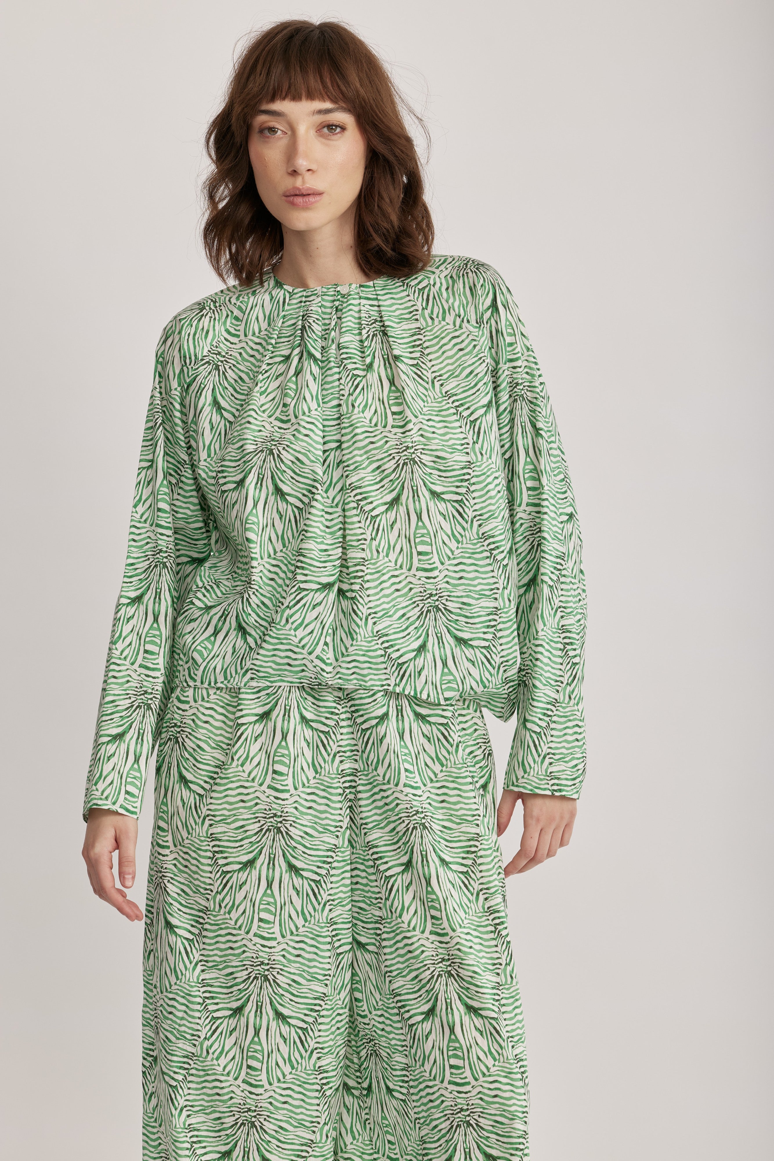 חולצה מבית המותג DRYKORN, מבד כותנה קליל בהדפס בגוון ירוק. החולצה בגזרה רחבה ונינוחה, עם שרוולים ארוכים, צווארון עגול עם קפלים מודגשים סביב הצוואר, וסגירת כפתור.הרכב: 100% כותנההדוגמנית בגובה 1.75 ולובשת מידה 2 של דרייקורן