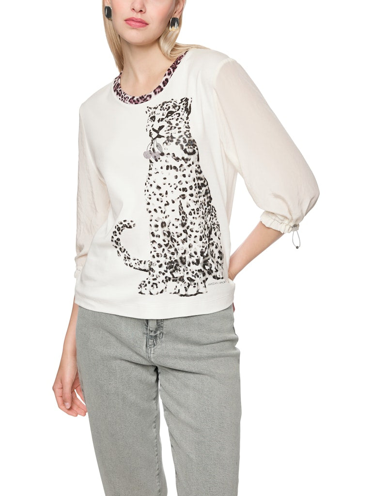 חולצה בגזרה ישרה ונינוחה, עשויה מבד כותנה גמיש ונעים, עם הדפס חזיתי של נמר, וצווארון עגול בגימור בד בדוגמה מנומרת. שרוולי החולצה באורך 3/4, מבד דק וזורם, עם חפתים אלסטיים הניתנים לכיוונון והתאמה אישית.הרכב: חולצה- 94% כותנה, 6% אלסטן, שרוולים- 59% פוליאסטר, 41% פוליאסטר ממוחזרהדוגמנית בגובה 1.79 ולובשת מידה 3 של מארק קיין 