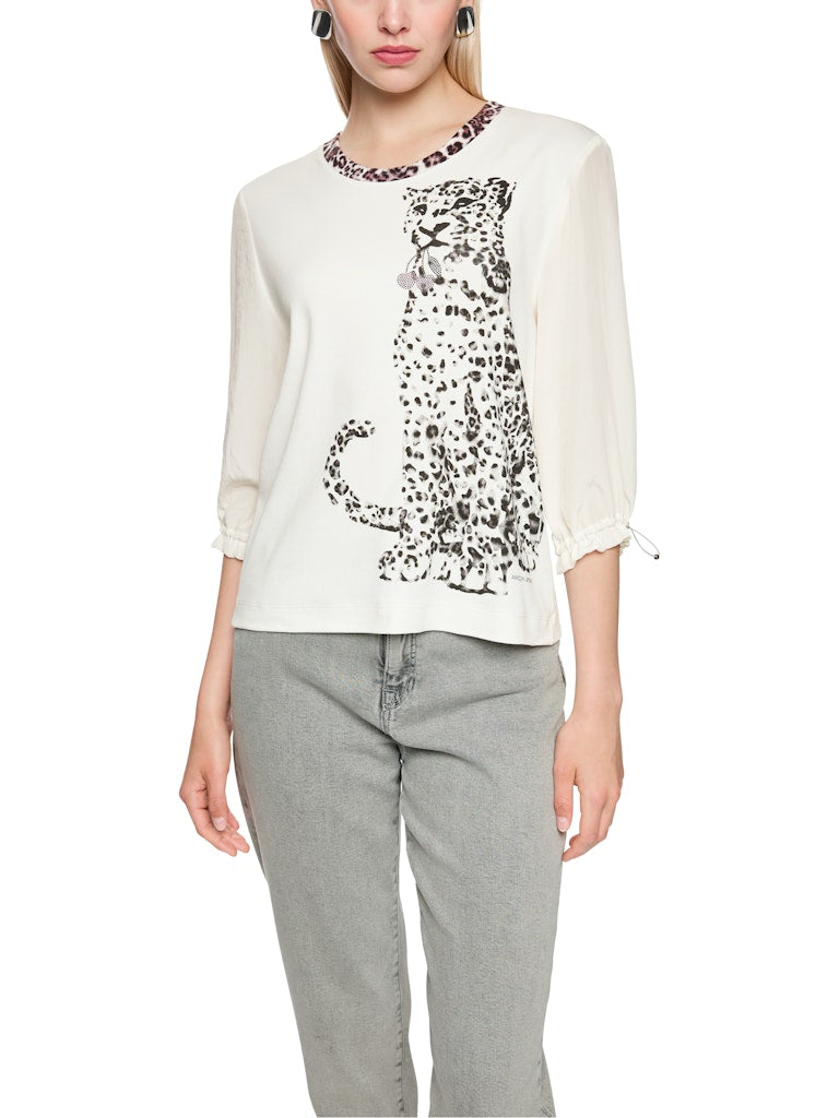 חולצה בגזרה ישרה ונינוחה, עשויה מבד כותנה גמיש ונעים, עם הדפס חזיתי של נמר, וצווארון עגול בגימור בד בדוגמה מנומרת. שרוולי החולצה באורך 3/4, מבד דק וזורם, עם חפתים אלסטיים הניתנים לכיוונון והתאמה אישית.הרכב: חולצה- 94% כותנה, 6% אלסטן, שרוולים- 59% פוליאסטר, 41% פוליאסטר ממוחזרהדוגמנית בגובה 1.79 ולובשת מידה 3 של מארק קיין 