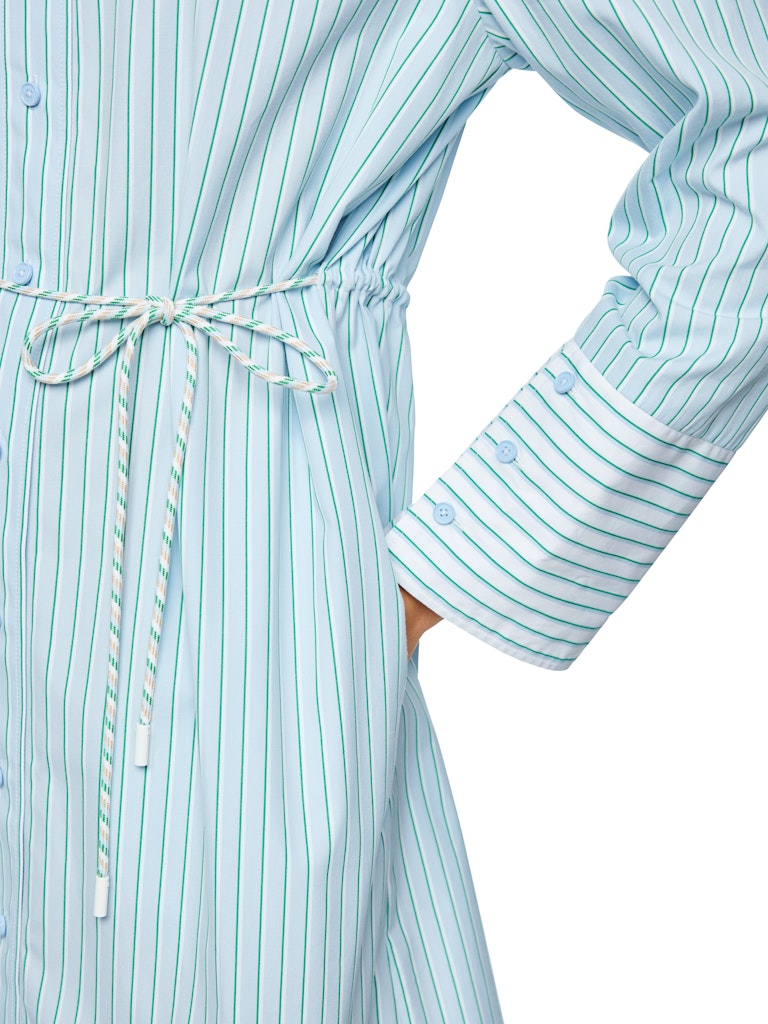 שמלת מיני בעיצוב קז'ואל-מודרני, בסגנון חולצה מכופתרת בדוגמת פסי סיכה בגוון ירוק, עשויה כותנה טהורה ונעימה במיוחד. גזרה רחבה ונינוחה, עם שרוך קשירה במותן, שרוולים ארוכים בסיומת חפתים מכופתרים רחבים המאפשרים התאמת אורך אישית, כיסי צד, וצווארון קלאסי.הרכב: 100% כותנההדוגמנית בגובה 1.79 ולובשת מידה 3 של מארק קיין