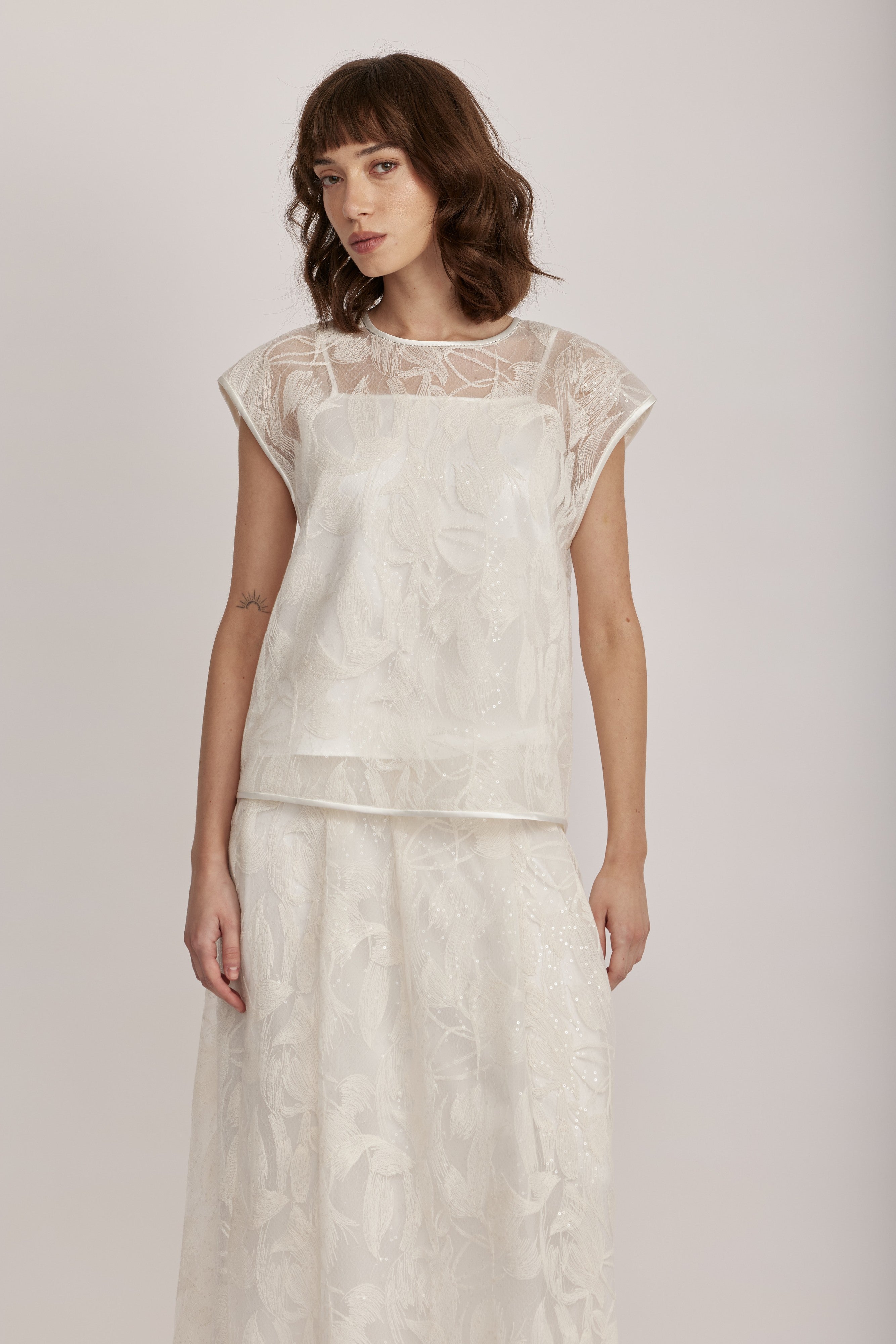 חולצה מקולקציית ה-Runway של המותג האיטלקי PESERICO, בעיצוב דו-שכבתי המשלב בד טול שקוף מעוטר ברקמה עדינה עם פאייטים בדוגמת עלים, ובד אורגנזה דק וקליל בגוון תואם, היוצר משחקי טקסטורה ושקיפויות, ומראה ייחודי.החולצה בגזרה ישרה ומשוחררת, עם שרוולי קאפ קצרים, צווארון עגול, בטנה פנימית, וסגירה באמצעות כפתור בגב.הרכב: טול- 50% פוליאמיד, 50% כותנה, אורגנזה- 100% פוליאסטר, בטנה- 97% פוליאסטר, 3% אלסטןהדוגמנית בגובה 1.75 ולובשת מידה 42 של PESERICO