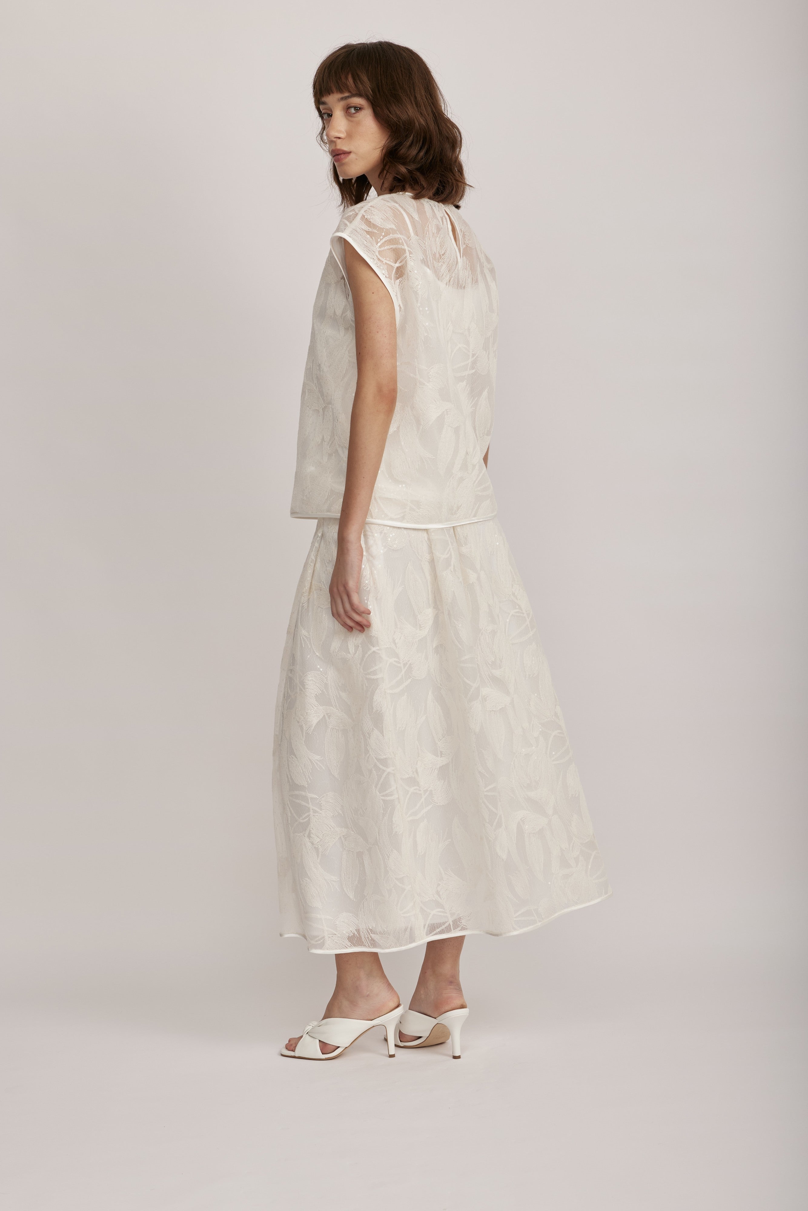 חצאית מקולקציית ה-Runway של המותג האיטלקי PESERICO, בעיצוב דו-שכבתי המשלב בד טול שקוף מעוטר ברקמה עדינה עם פאייטים בדוגמת עלים, ובד אורגנזה דק וקליל בגוון תואם, היוצר משחקי טקסטורה ושקיפויות, ומראה ייחודי.החצאית באורך מידי, בגזרה מתרחבת ונינוחה, עם קפלים מודגשים, בטנה פנימית, וסגירה באמצעות רוכסן צידי נסתר.הרכב: טול- 50% פוליאמיד, 50% כותנה, אורגנזה- 100% פוליאסטר, בטנה- 97% פוליאסטר, 3% אלסטןהדוגמנית בגובה 1.75 ולובשת מידה 42 של PESERICO