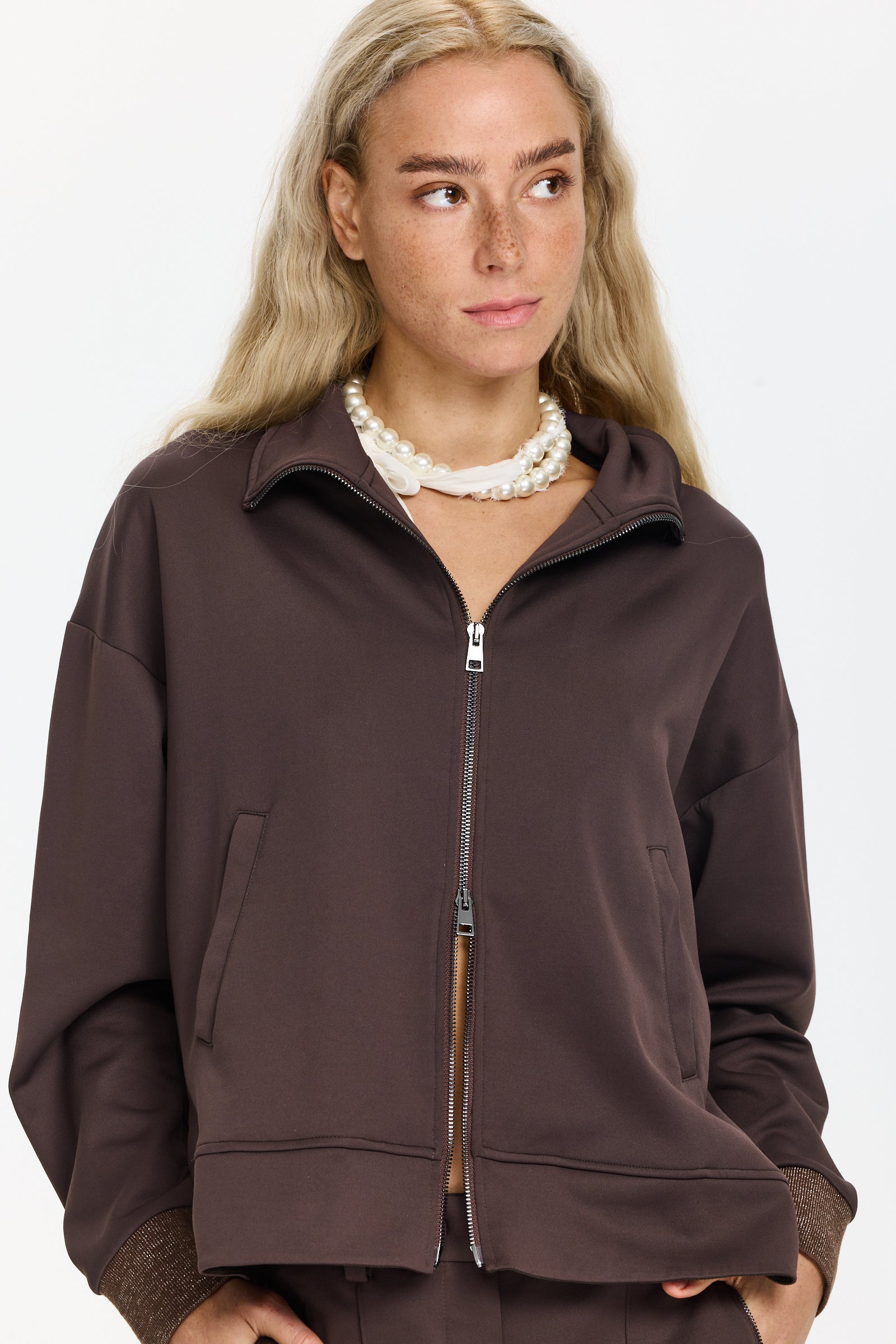 סווטשירט בצבע חום כהה עם צווארון גבוה, רוכסן כפול, כיסים קדמיים וכוכב בגב, קצוות השרוולים נוצציםהדוגמנית בגובה 1.75 ולובשת מידה 40 של Lorena Antoniazzi