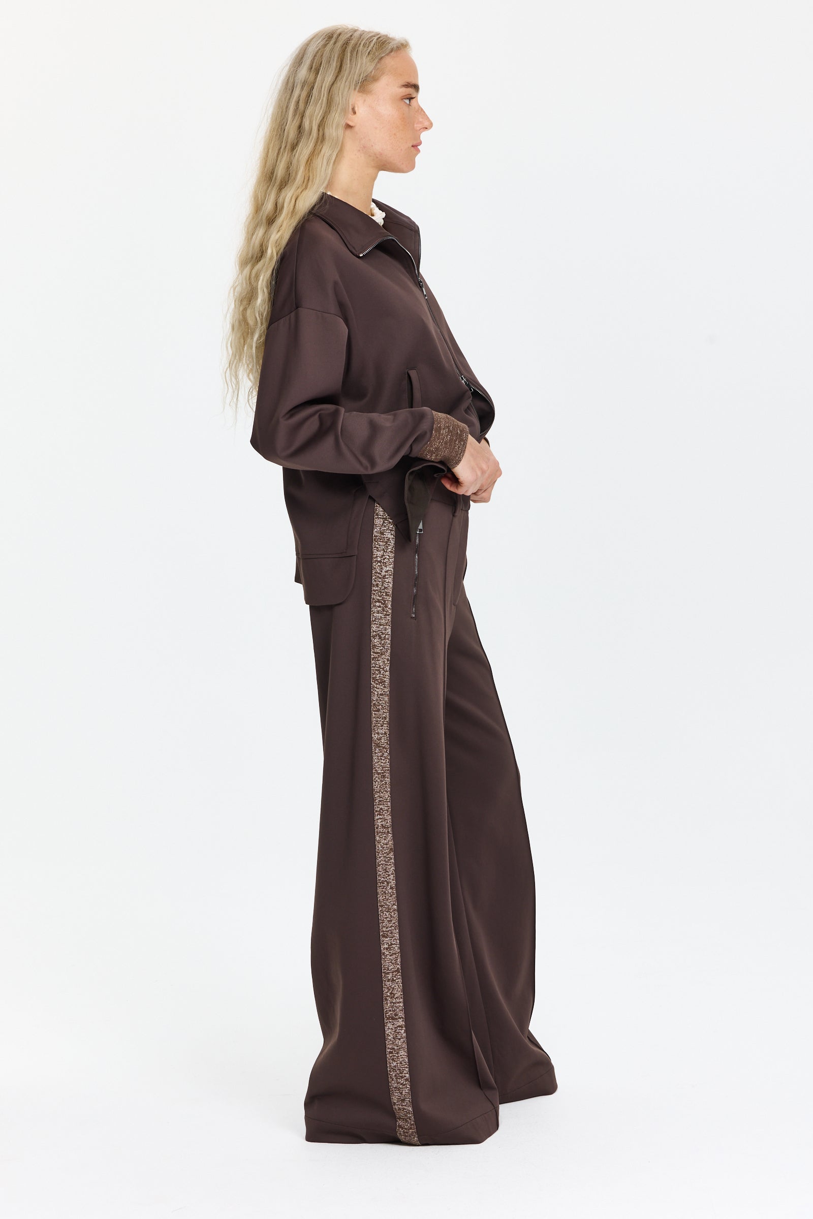 מכנסיים רחבים בצבע חום כהה עם כיסים צדדיים, מעוטרים בפסים מנצנצים לאורך הצדדיםהדוגמנית בגובה 1.75 ולובשת מידה 42 של Lorena Antoniazzi